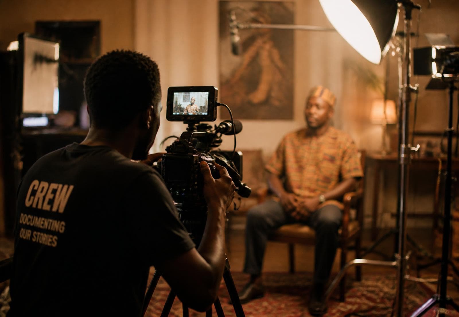 A camera operator filming a seated interview on a lit set
